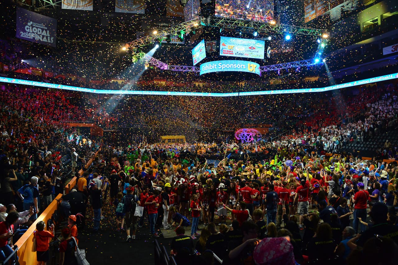 A large crowd gathers in an arena with colorful flags and bright lights.