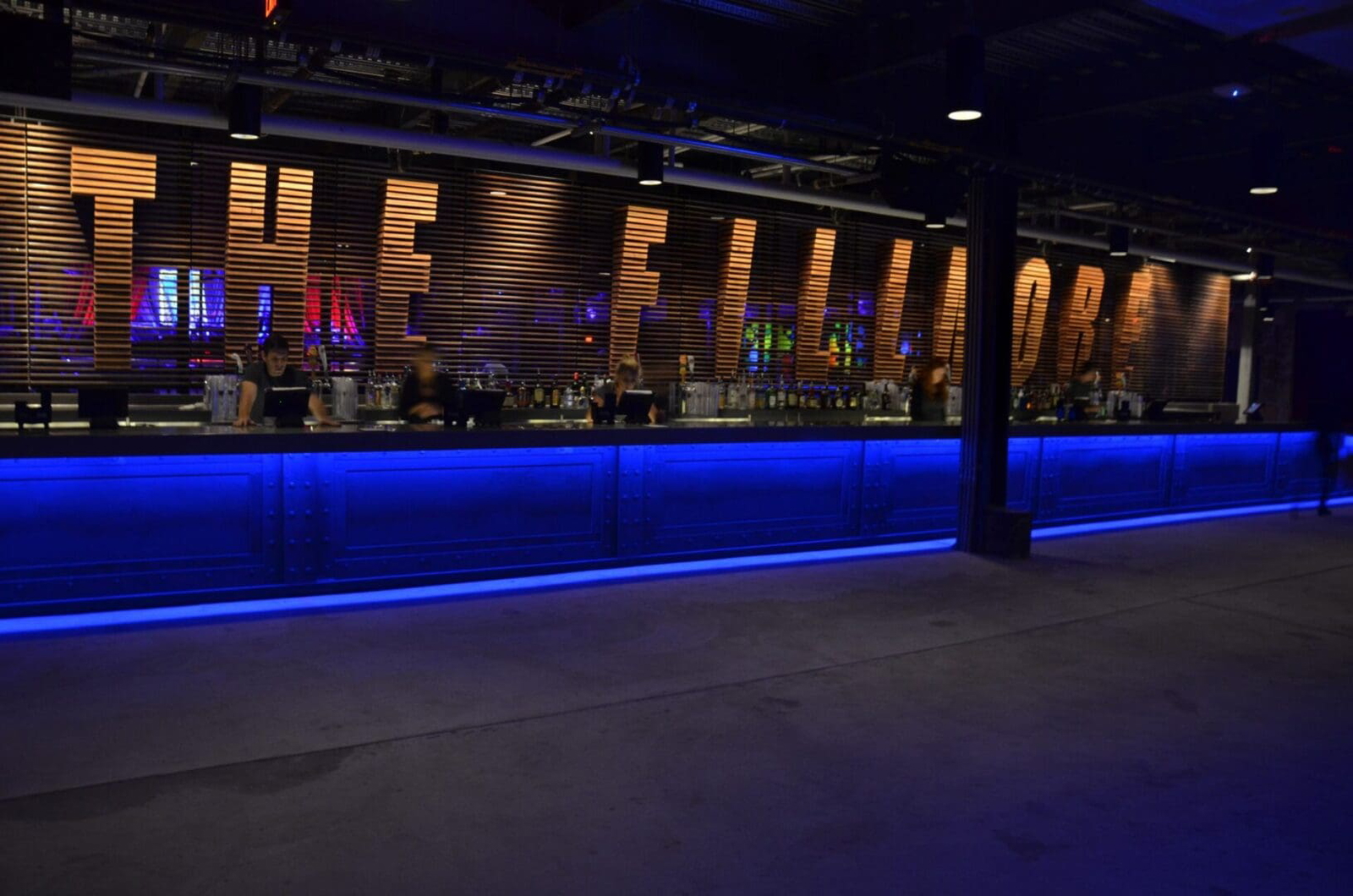 A dimly lit bar with blue LED lighting under the counter and bottles displayed on shelves.