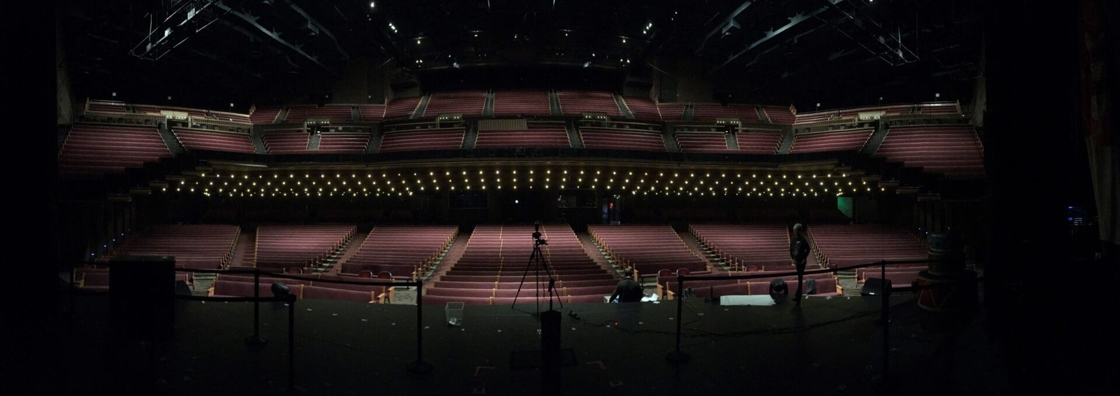 Empty theater stage with rows of red seats and dim lighting.