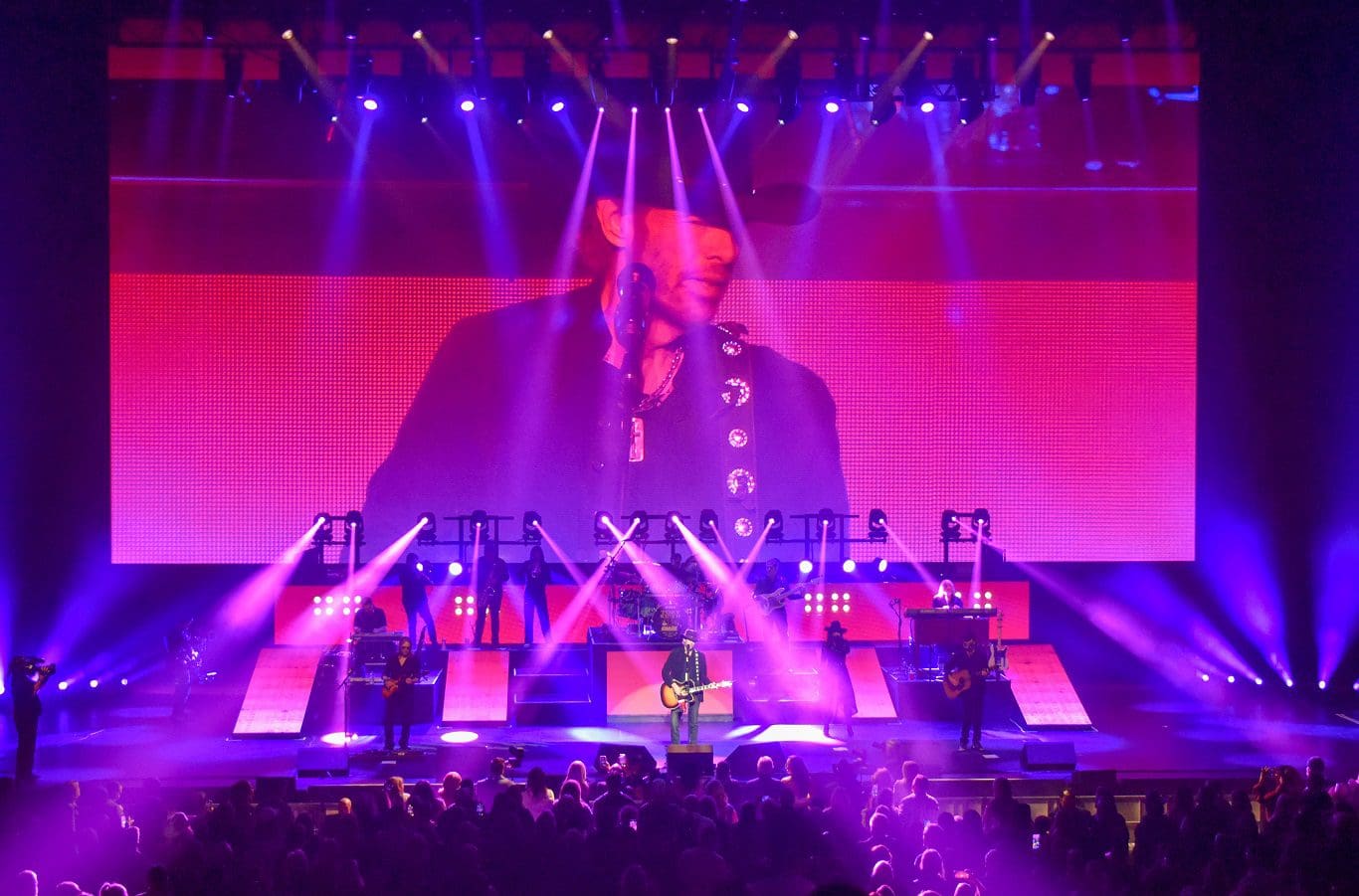 A vibrant concert stage with colorful lights and a large screen showing the performer.