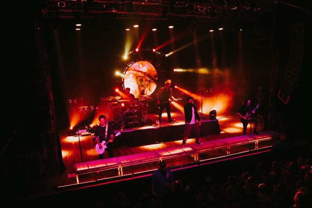 A band performs on stage with vibrant orange and red lighting effects.