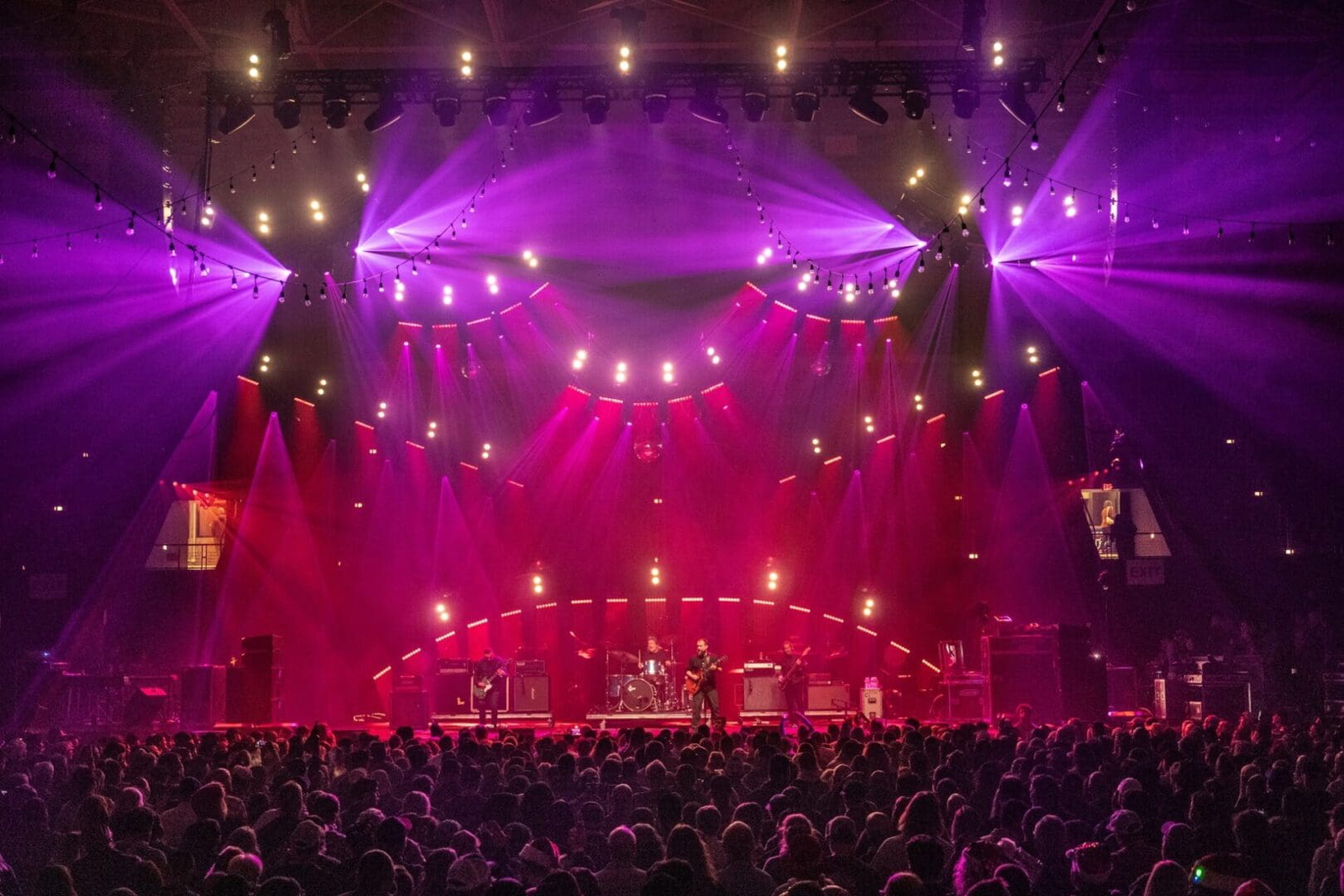 A vibrant concert stage with purple lighting and a large audience.