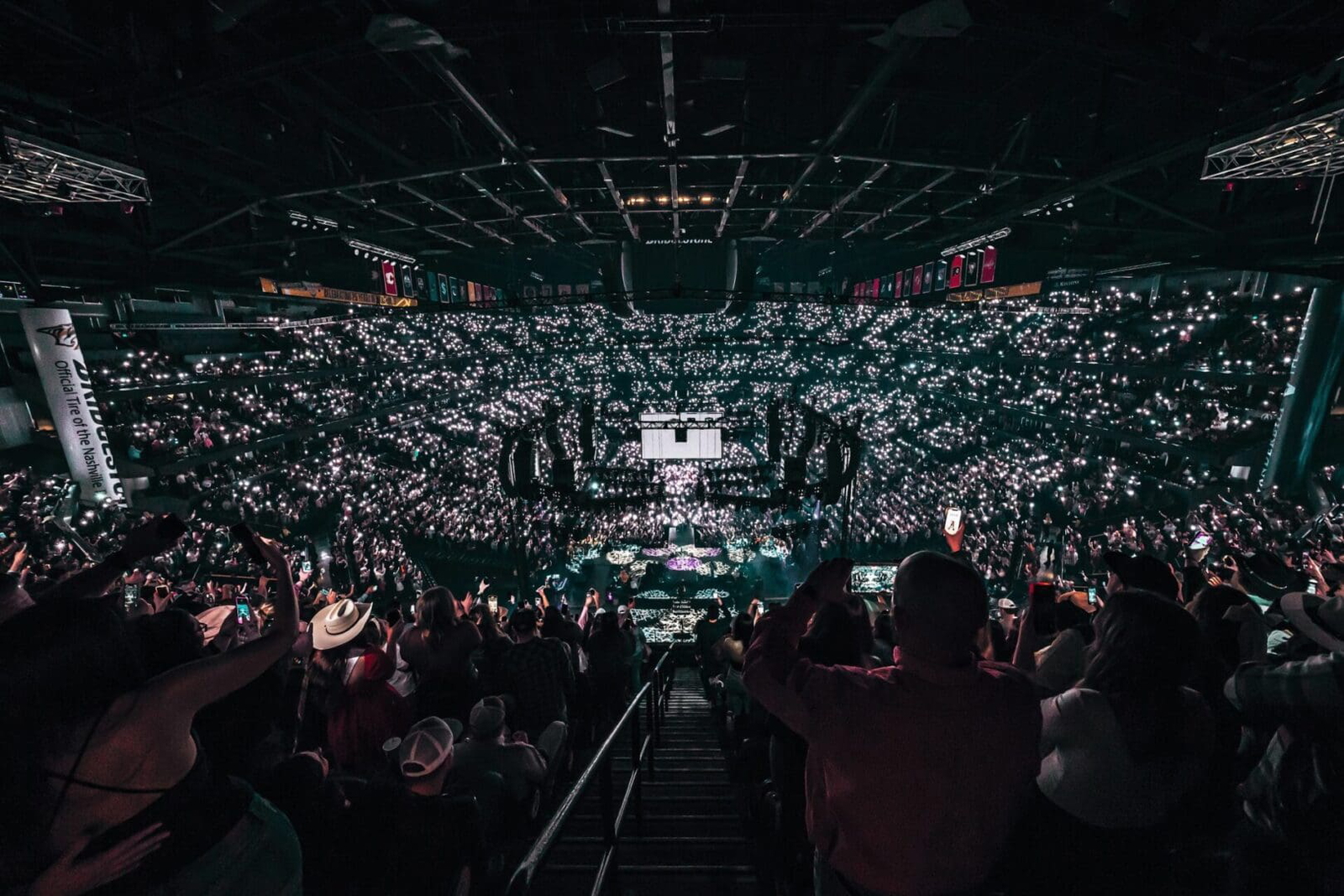 A packed indoor arena with an enthusiastic crowd holding up lights.