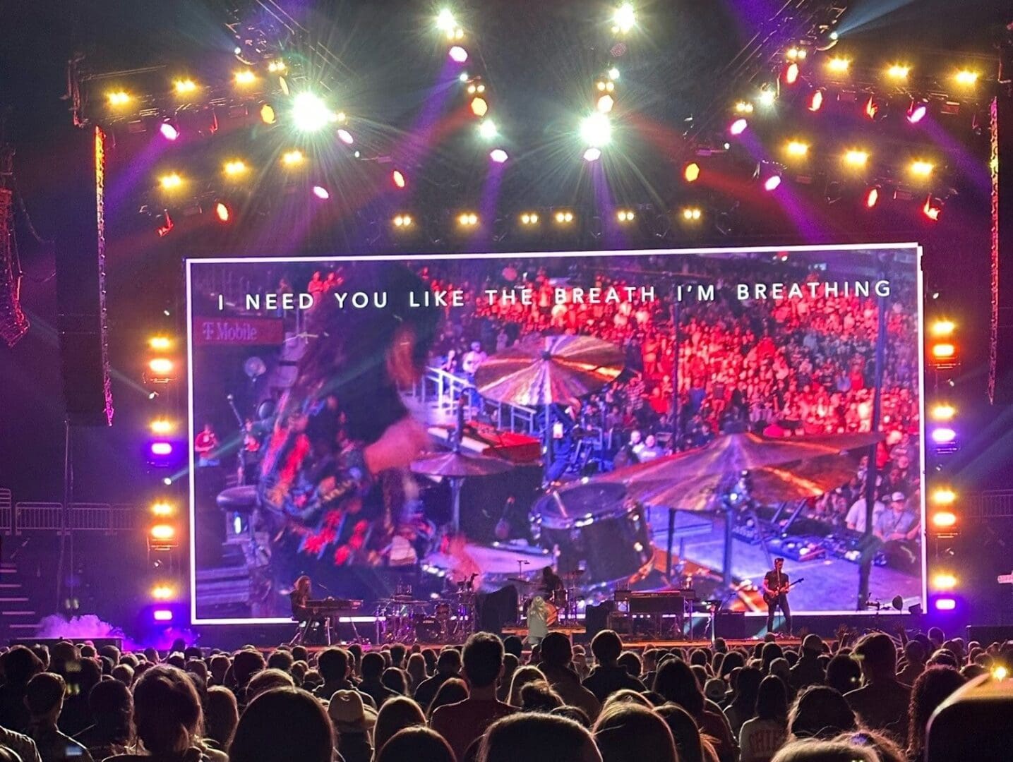 A vibrant concert stage with bright lights and large screens displays colorful visuals.