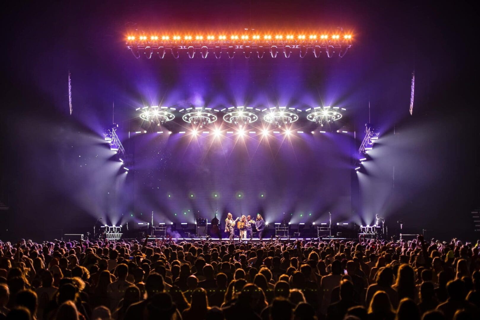 A vibrant concert scene with bright stage lights and a large enthusiastic crowd.