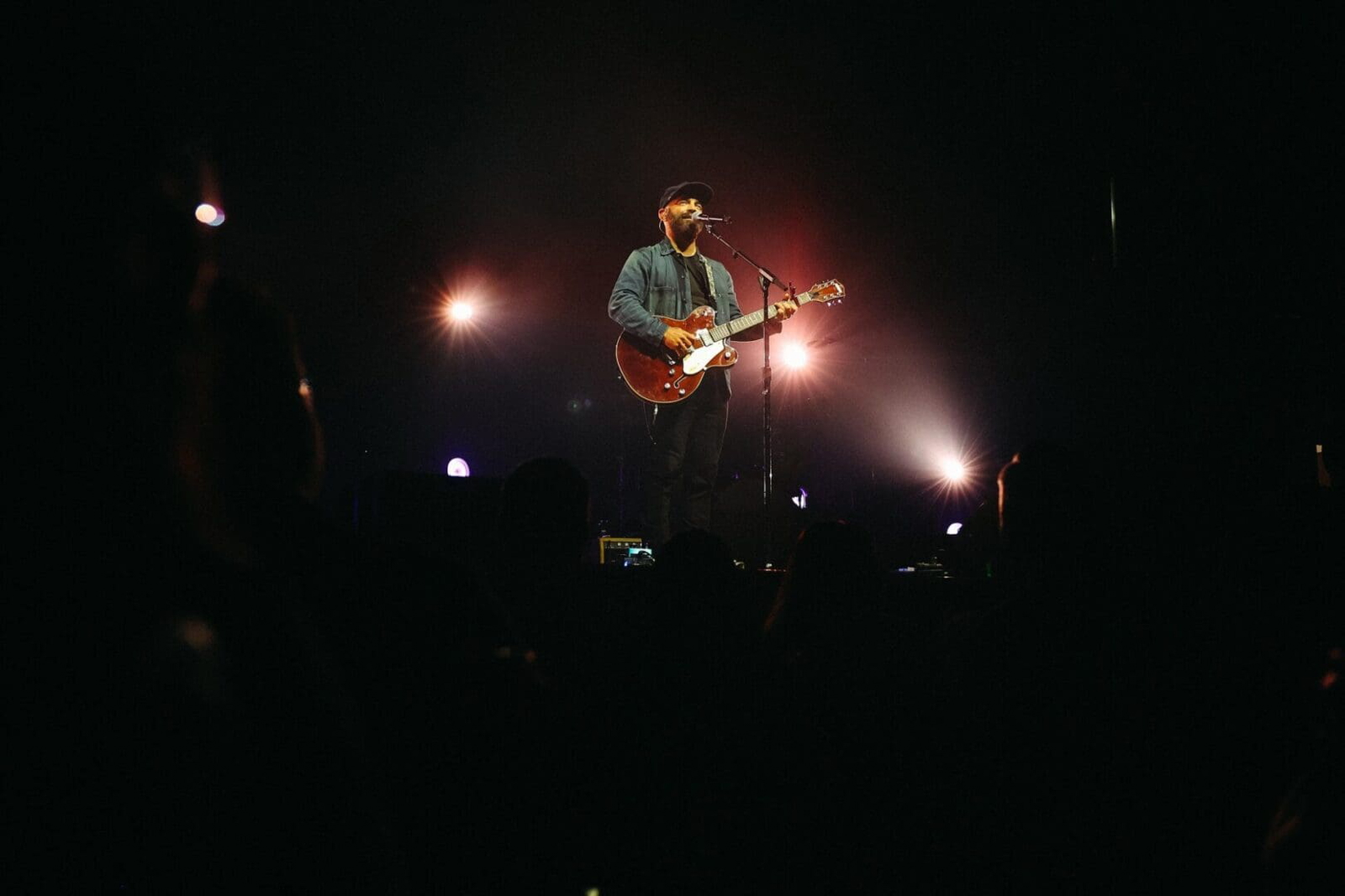 Musician playing guitar on stage with dramatic lighting.