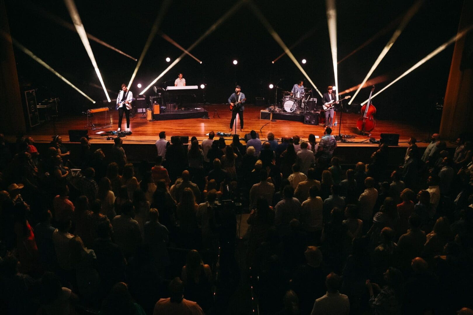 A band performing live on stage with lights and a large audience.