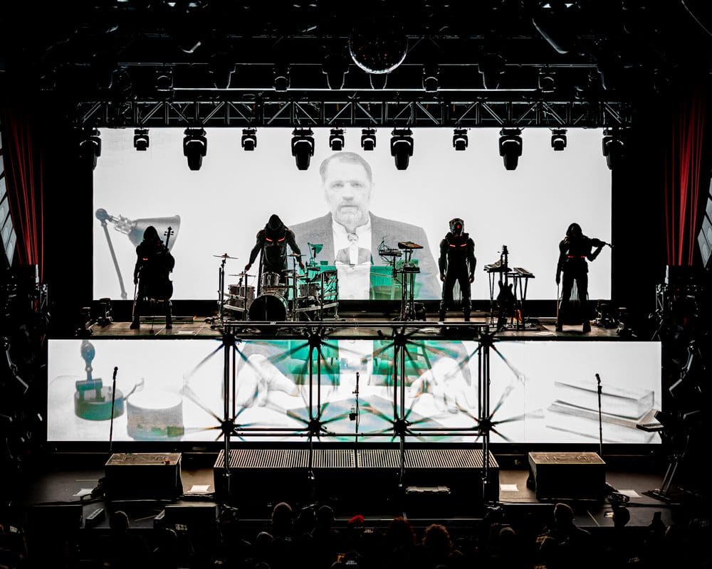 Silhouetted band performing with a large black-and-white video projection behind them.