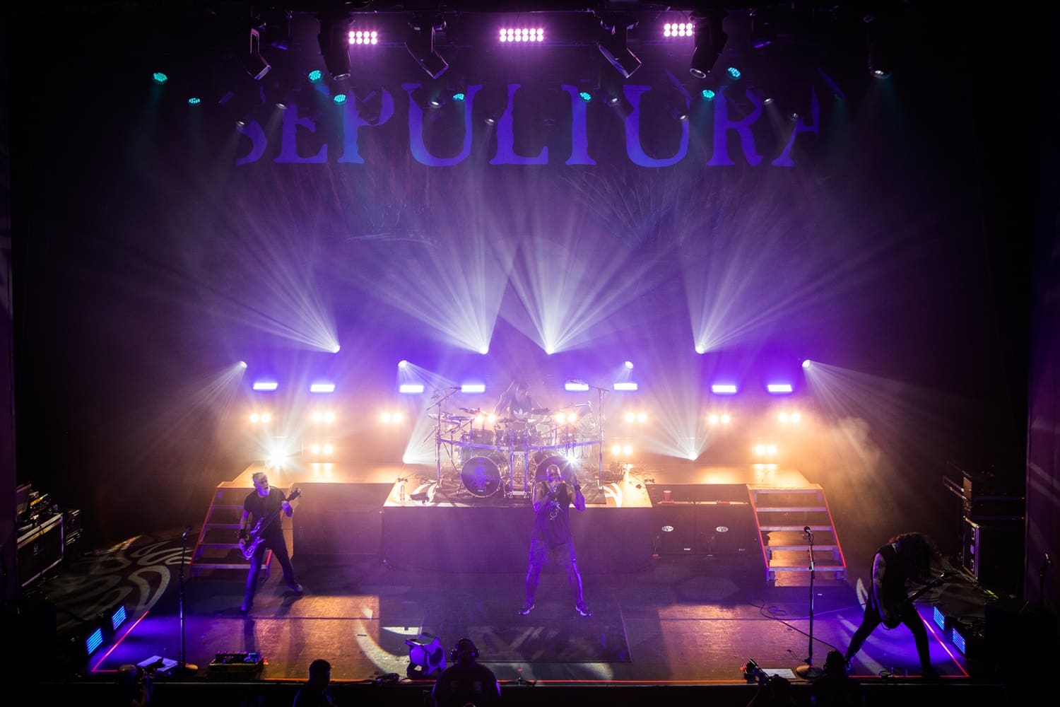 Live band performing on a vibrant stage with purple and yellow lighting.