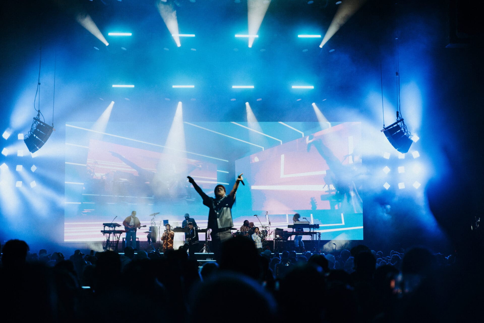 Silhouetted singer performs energetically on a brightly lit stage.