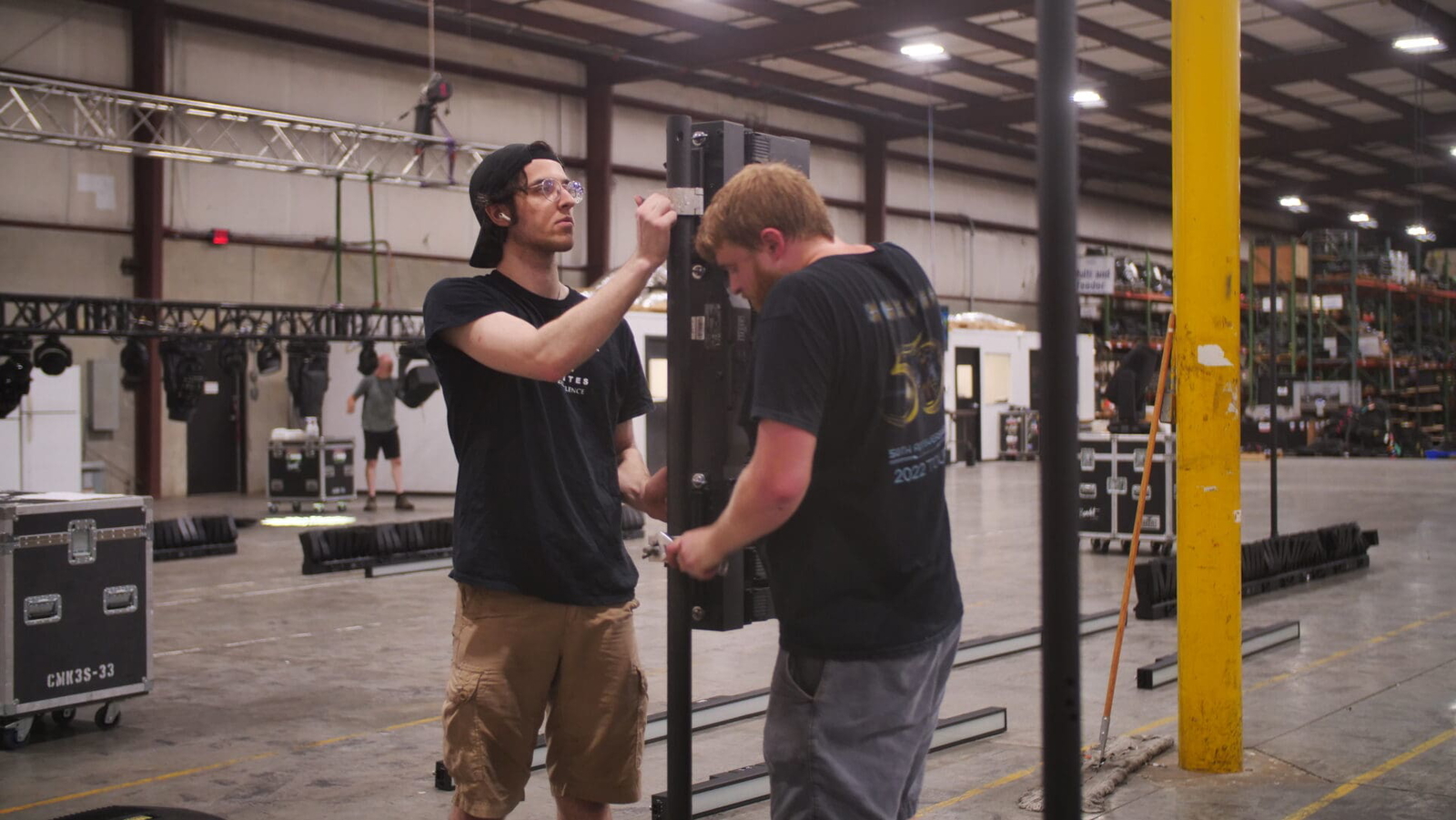 Two men setting up audio equipment in an industrial space.