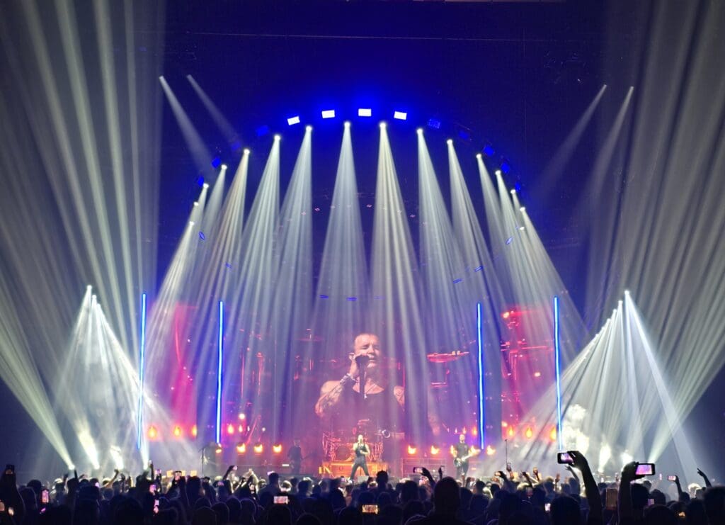 A singer performs onstage with dramatic lighting and a large crowd.
