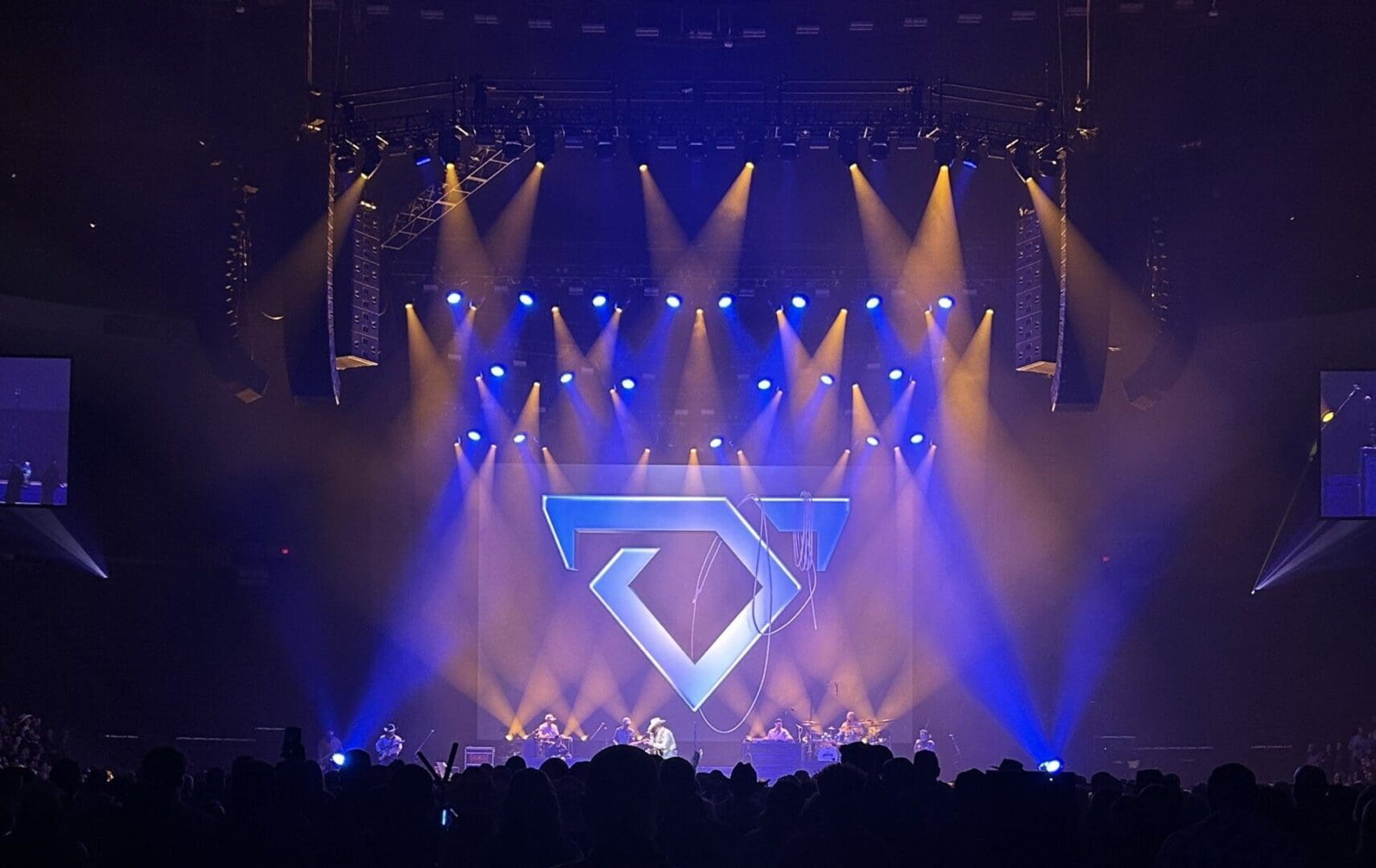 A vibrant concert stage with blue and purple lights illuminating a large geometric symbol.