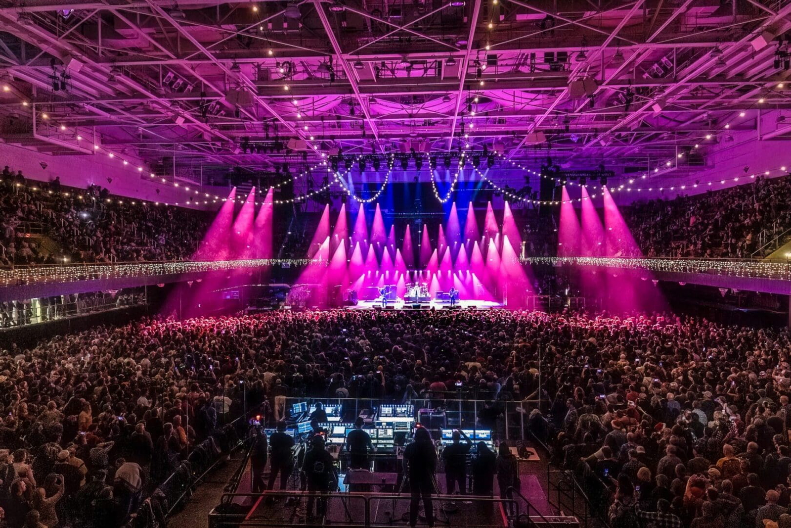 A vibrant concert with pink and purple stage lights and a large crowd.