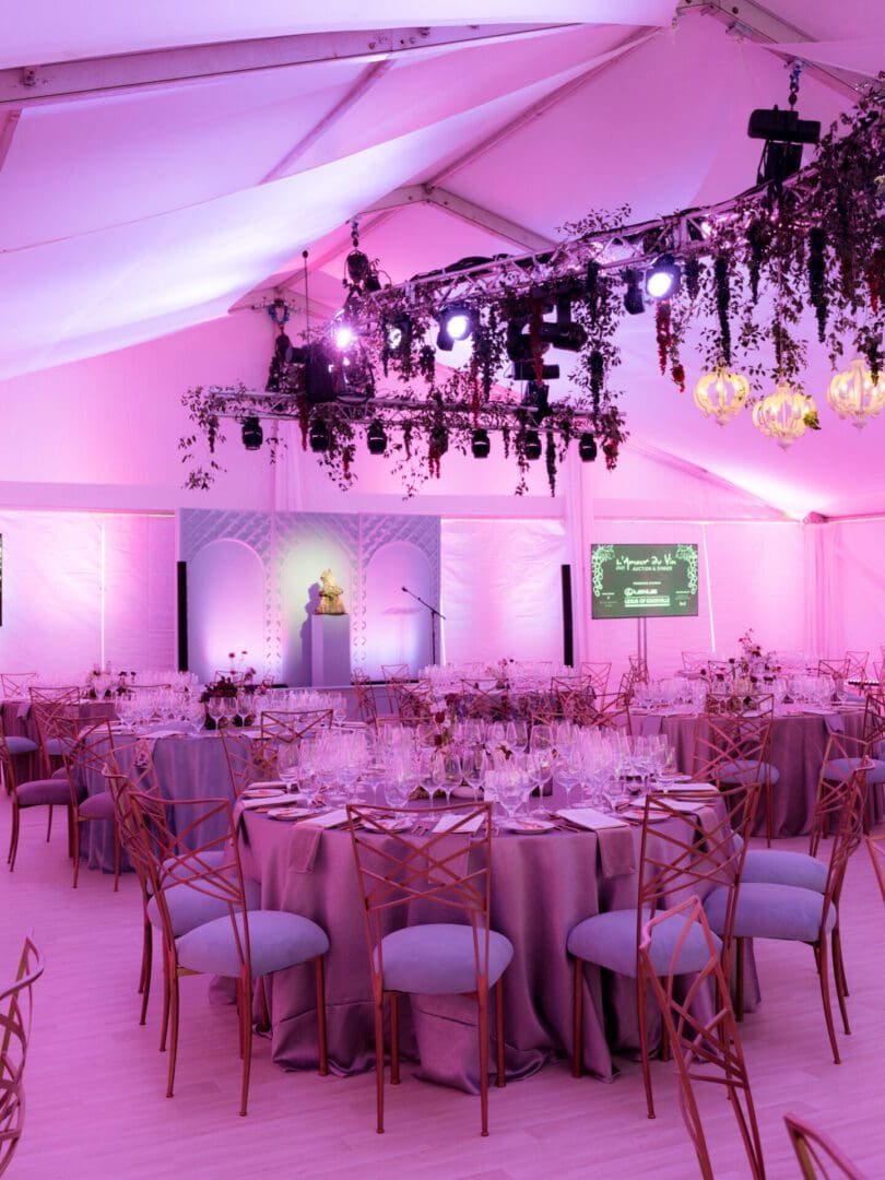 Elegant wedding reception setup with soft pink lighting and decorated tables.
