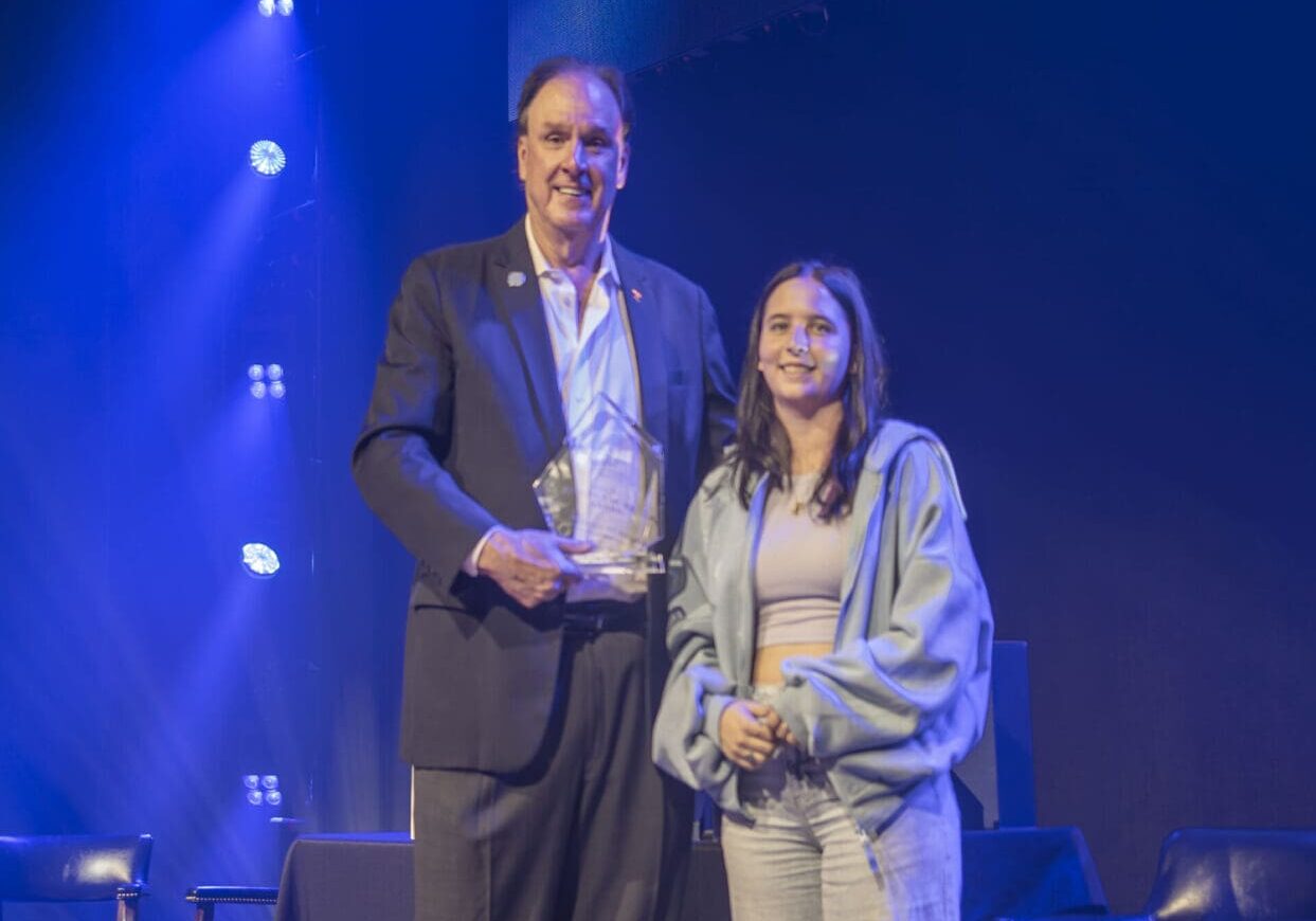 Two people holding awards on stage under blue lights. Two people holding awards on stage under blue lights.