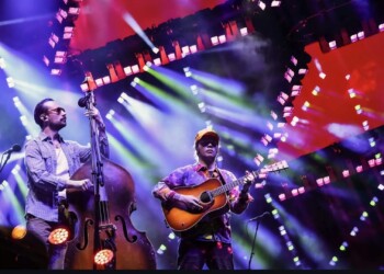 Musicians perform on stage with colorful lights and smoke effects.