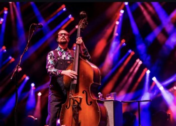 Musician playing double bass on stage with colorful lights.