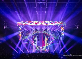 Colorful light show with vibrant purple and blue beams over a concert stage.