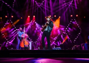 A lively band performs on stage with vibrant purple and orange lighting.