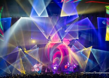 Colorful geometric light show with a live band on stage.