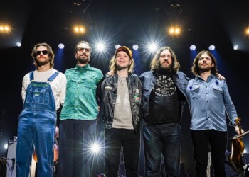 A band stands together on stage under bright lights.