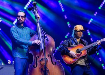 Two musicians playing upright bass and acoustic guitar on stage with colorful lights.