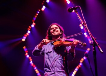Musician playing violin on stage with colorful lights.