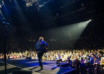 Performer on stage illuminated by spotlight in front of a large audience.