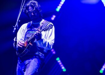 Musician playing guitar on a blue-lit stage.