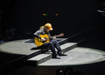 Musician playing acoustic guitar on stage under spotlight.