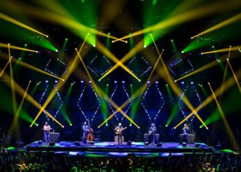 Dancers perform on a stage with vibrant green and yellow lights.