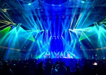 Bright blue and green stage lights illuminate a concert crowd.