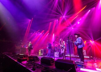 Band performing live on a vibrant purple-lit stage.