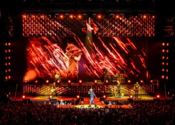 A singer performs on a brightly lit stage with vibrant red and orange lighting.