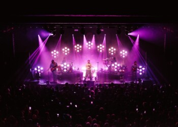A vibrant concert scene with a singer illuminated by purple stage lights.