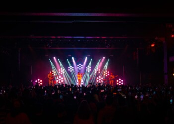 Colorful lights illuminate a concert stage with a crowd below.