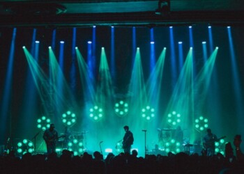 A performer sings on stage with vibrant blue and green lights.