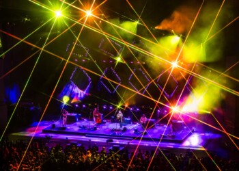 Photo: Jesse Faatz Colorful laser lights illuminate a lively concert stage with a large crowd.