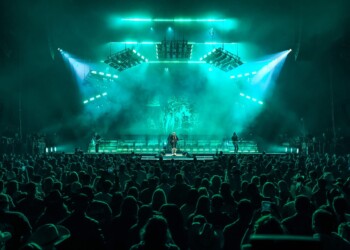A vibrant concert scene with bright teal lighting and a packed audience.