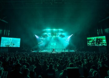 A vibrant live concert with blue-green lighting and a large crowd.
