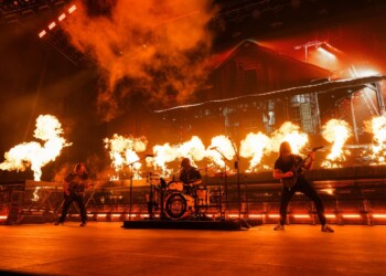 A band performs energetically amidst a stage filled with fiery pyrotechnics.