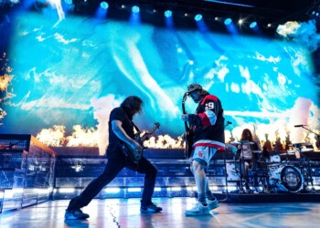 Two musicians perform energetically on a brightly lit stage.