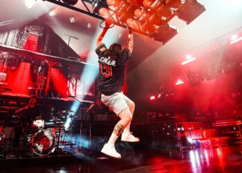 Energetic performer jumping mid-air during a live concert with vibrant stage lights.