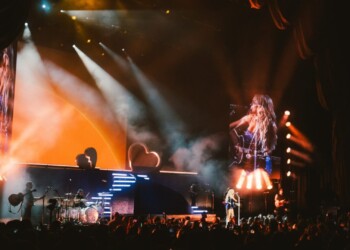 A female singer performs energetically on stage with vibrant lighting and a musician at the keyboard.