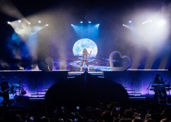 A singer performs on stage with dramatic lighting and a large moon backdrop.