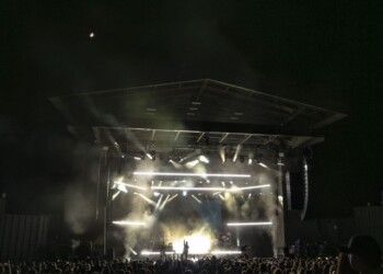 A night concert with bright stage lights and a crowd in front.