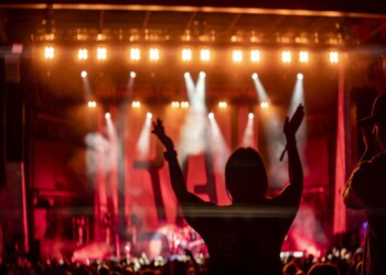 Silhouette of a person cheering at a vibrant concert with bright stage lights.