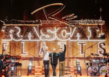Four musicians perform on stage under bright lights with a large "Rascal Flatts" sign.