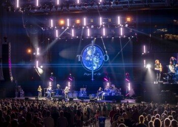 A live band performs on stage with vibrant lights and a large crowd.